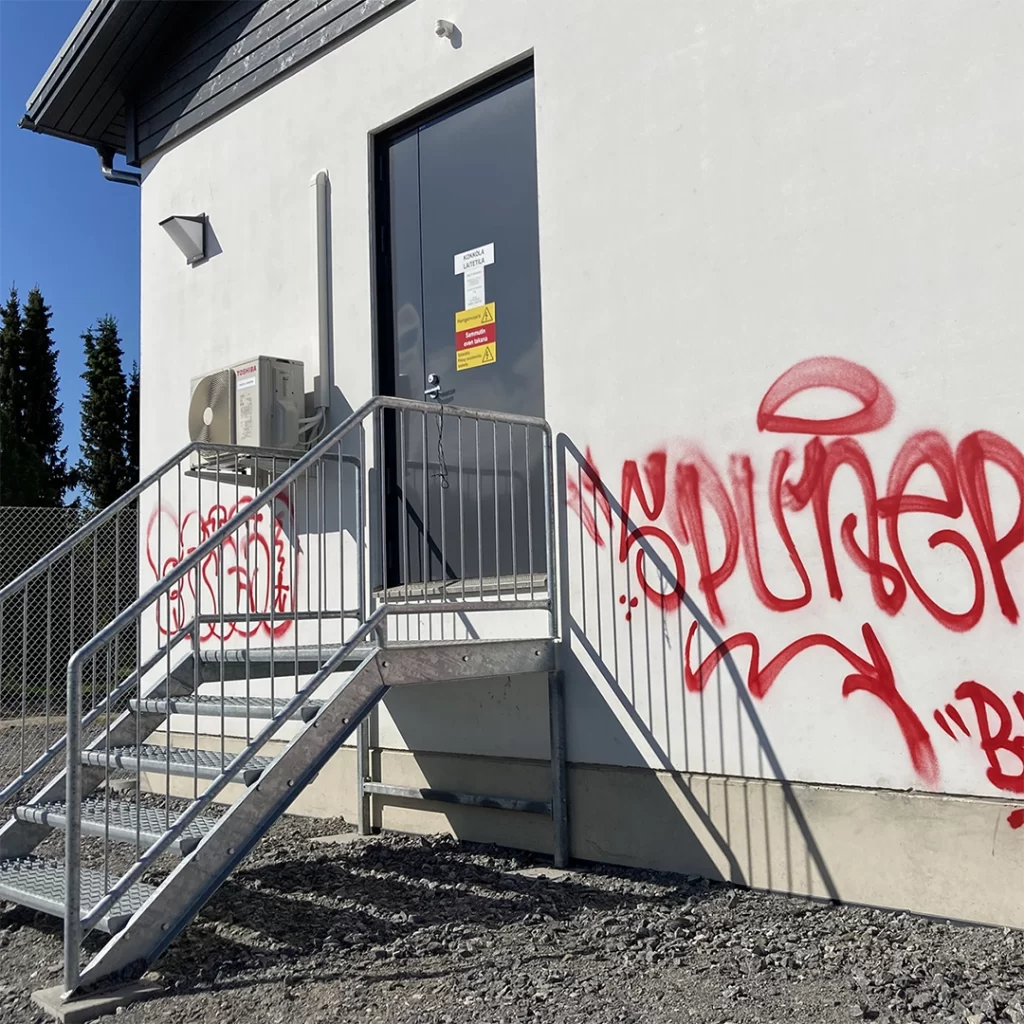 Valkoinen pieni rakennus jossa on punainen graffiti seinässä